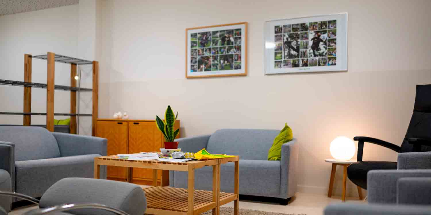 Pausenraum der Kita mit kleinen Couchen und Sesseln, einem Holzisch in der Mitte und zwei großen Rahmen mit Fotos aus der Kita.